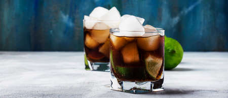 Alcoholic cocktail cuba libre with ice, lime, juice, cola and golden rum, gray bar counter...