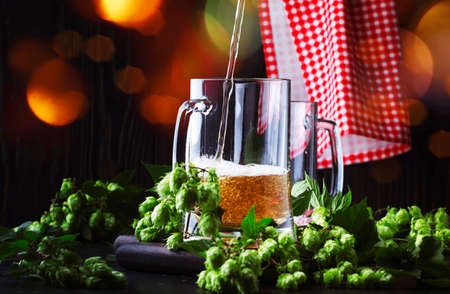 Two glasses of german light beer, beer poured into mug, dark bar counter, selective focus