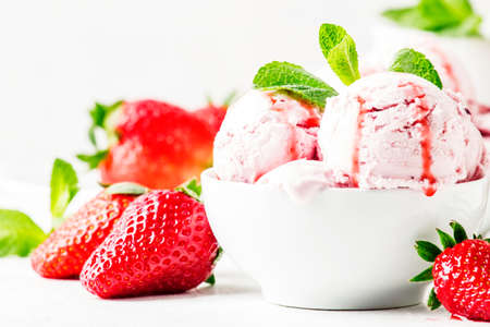 Strawberry ice cream with jam topping, decorated with green mint leaves, gray background, selective focusの写真素材