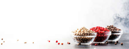 Pepper set. Black, white and pink rose peppers in bowls, assorted spices on gray kitchen table,...