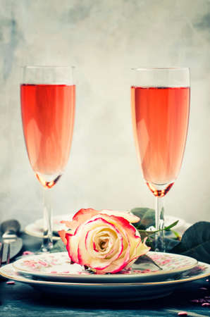 Festive table setting for valentines day, plates and glasses with pink champagne for couple of lovers, gray background, selective focusの写真素材