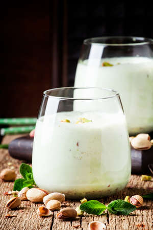 Pistachio milk cocktail with ice cream, nut and green mint, old wooden background, selective focusの写真素材