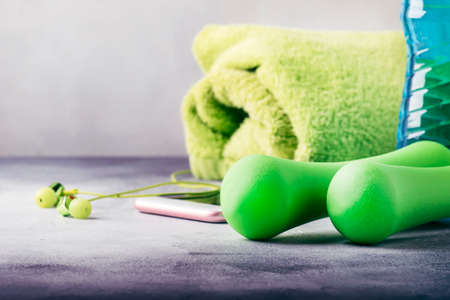 Female fitness concept: green dumbbells, isotonic blue water, smartphone with headphones and towel on gray concrete floor, selective focusの写真素材