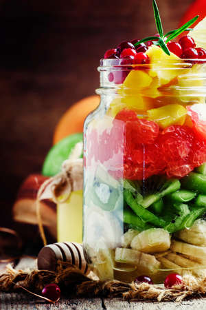 Exotic fruit salad with banana, kiwi, grapefruit, mango, cranberry and lemon juice and honey, served in a glass jar. Vintage wooden background, selective focusの写真素材