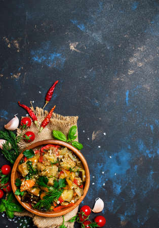 Stewed aubergines with vegetables in a bowl, dark background, top viewの写真素材