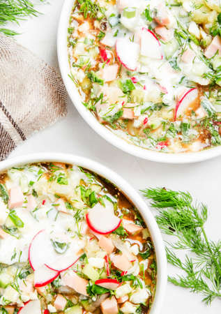 Traditional Russian summer cold soup with vegetables, herbs and meat products, white background, top...
