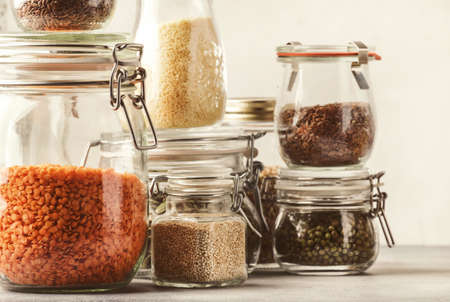 Stocks or set of cereals, pasta, groats, organic legumes and useful seeds in glass jars. Vegan source of protein and energy resources. Healthy vegetarian food. Domestic life scene. Gray kitchen table background. Selective focusの写真素材