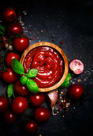 Hot tomato ketchup sauce with garlic, spices and green basil with cherry tomatoes in wooden bowl on...