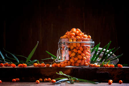 Fresh sea buckthorn in a glass jar. Vintage wooden background, low key. Selective focus
