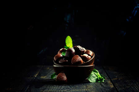 Chocolate candies, assorted, decorated with mint leaves, dark background, low key, selective focusの写真素材