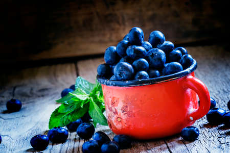 Ripe blueberries in red enamel mug, vintage wooden background, rustic style, selective focus