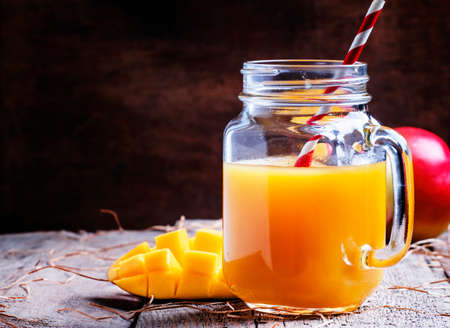 Mango juice in a large glass jar and fresh fruits, vintage wooden background, selective focusの写真素材