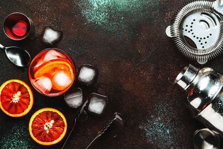 Fashionable alcoholic cocktail Negroni with dry gin, red vermouth and red bitter, orange and ice cubes. Brown bar counter background, bar tools, top view, place for text.の写真素材