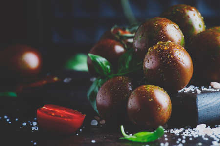 Brown cherry tomatoes with sea salt and green basil on dark table, autumn harvest, selective focusの写真素材