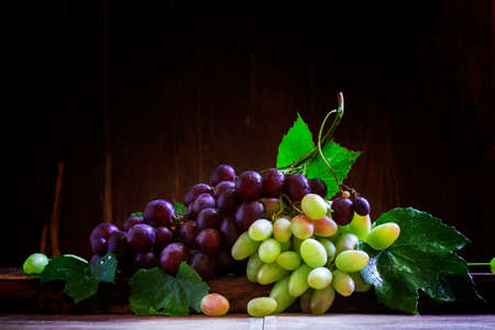 Local grapes of southern Russia and North Caucasus. Green and purple berries with leaves. Vintage wooden background. Low key, selective focus.の写真素材