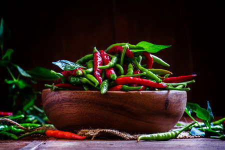 Red and green hot peppers in a wooden bowl. Low key, selective focusの写真素材