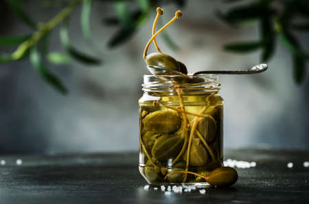 Capers. Marinated or pickled canned capers fruit close up in glass jar on gray kitchen table background. Copy spaceの写真素材