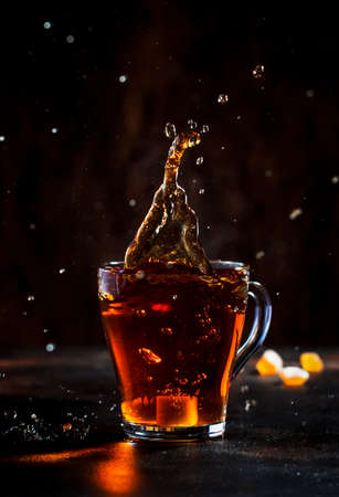 Splash in glass cup of black tea with natural steam on brown backgroundの写真素材