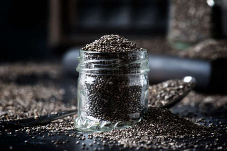 Chia seeds in small glass jar, gray background, selective focusの写真素材