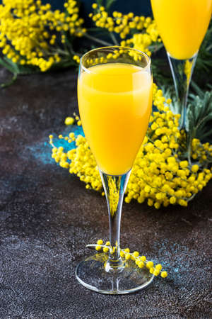 Low alcohol cocktail mimosa with orange juice and cold dry champagne or sparkling wine in glasses, blue background with flowers, place for text, selective focusの写真素材