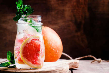 Grapefruit soda water with ice and mint leaves, vintage wooden background, selective focusの写真素材