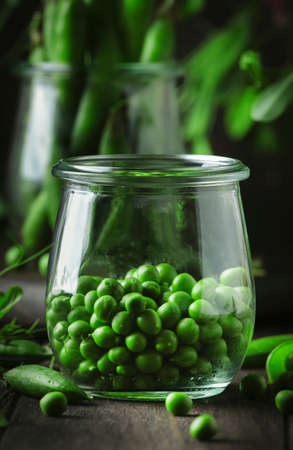 Peeled fresh sweet green peas in glass jar, dark wooden kitchen table background, copy space, selective focusの写真素材