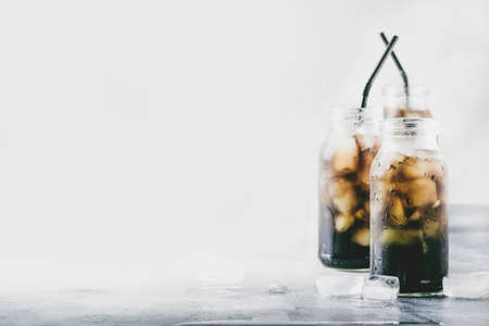 Healthy drinks concept: cold black detox mineral water with crushed ice in glass bottles, with...