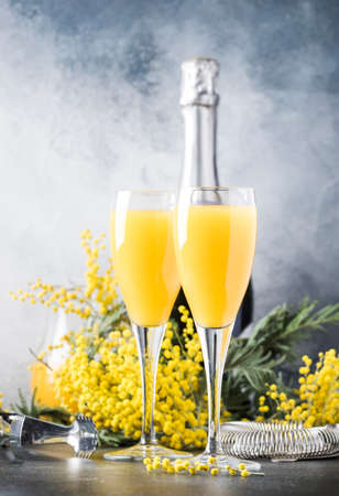 Festive alcohol cocktail mimosa with orange juice and cold dry champagne or sparkling wine in glasses, gray bar counter background with flowers, place for text, selective focusの写真素材