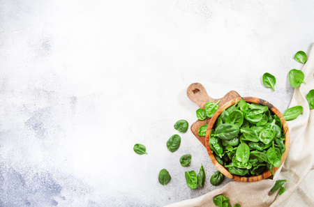 Fresh baby spinach leaves in wooden bowl on gray stone table. Top view, copy space