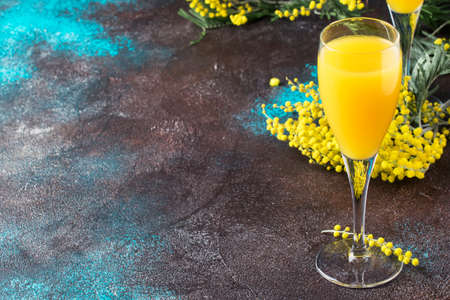 Low alcohol cocktail mimosa with orange juice and cold dry champagne or sparkling wine in glasses, blue background with flowers, place for text, selective focusの写真素材