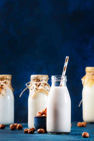 Vegan Hazelnut nut milk in bottles, closeup, blue table background. Non dairy alternative milk....