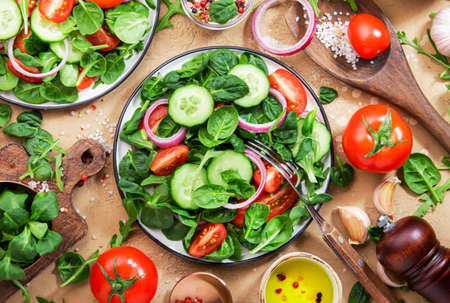 Spring vegan salad with spinach, cherry tomatoes, corn salad and red onion. Healthy food concept. Beige stone table background. Top viewの写真素材