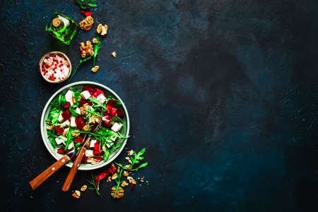 Arugula, Beet and cheese salad with fresh radicchio and walnuts on plate with fork, dressing and spices on blue kitchen table background, place for text, top viewの写真素材