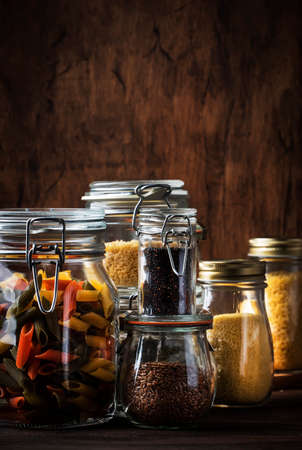 Stocks or set of cereals, pasta, groats, organic legumes and useful seeds in glass jars. Vegan source of protein and energy resources. Healthy vegetarian food. Domestic life scene. Rustic wooden kitchen table background. Selective focusの写真素材