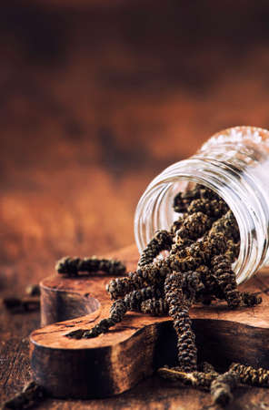 Fragrant long pepper spilling out of glass jar, vintage kitchen table background, selective focusの写真素材