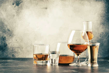 Selection of hard strong alcoholic drinks in big glasses and small shot glass in assortent: vodka, cognac, tequila, brandy and whiskey, grappa, liqueur, vermouth, tincture, rum. Gray bar counter background, selective focus, vintage toned imageの写真素材