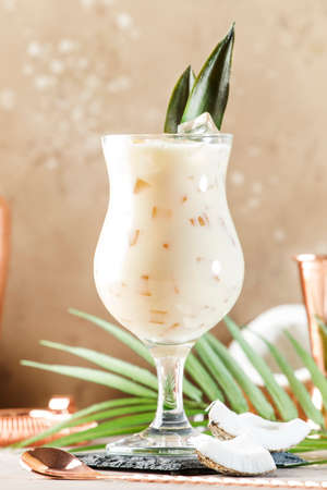 Pina Colada Cocktail on sand beige background with tropical fruits and bar tools, summer relaxation...