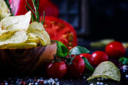 Gold salted potato chips with rosemary on black stone background with vegetables, spices and basil, selective focusの写真素材
