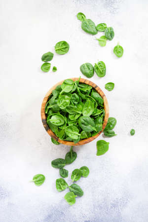 Fresh baby spinach leaves in wooden bowl on gray stone table. Top view, copy spaceの写真素材