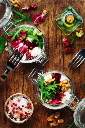Beet salad with fresh arugula, soft goat cheese and walnuts, trendy salad jar, steel fork, gray kitchen table background, wooden cutting board, copy space, top viewの写真素材