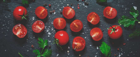 Cut cherry tomatoes on a black background with spices, top view and toned imageの写真素材