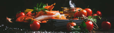 Ingredients for the preparation black pasta with seafood, tomatoes and white dry wine, black food cooking background, still life, banner, selective focusの写真素材