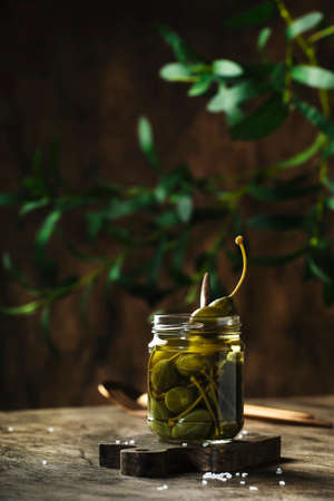 Capers. Marinated or pickled canned capers fruit in glass jar on wooden table background. Space for textの写真素材