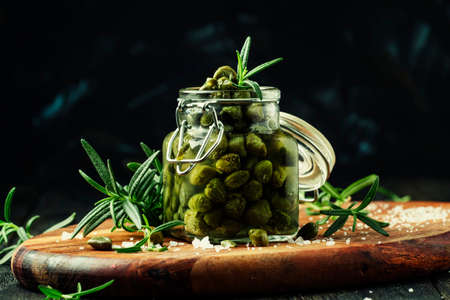 Capers with vinegar, salt and rosemary on a dark background, selective focusの写真素材