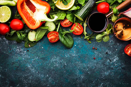 Fresh helthy food cooking or salad making ingredients on dark background with rustic wooden board. Diet or vegetarian food concept. Top view, copy spaceの写真素材