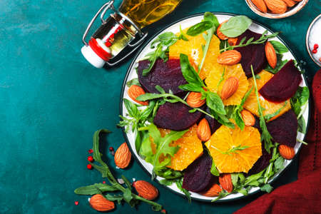 Fresh Beetroot Salad with Orange, arugula and almonds nut on blue background. Vegan healthy summer food. Flat lay. Copy spaceの写真素材