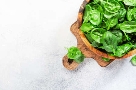 Fresh baby spinach leaves in wooden bowl on gray stone table. Top view, copy spaceの写真素材