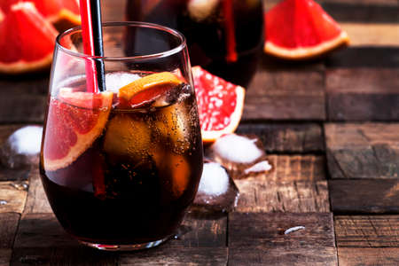 Alcoholic cocktail with cola, grapefruit juice and ice, dark wood background, selective focusの写真素材