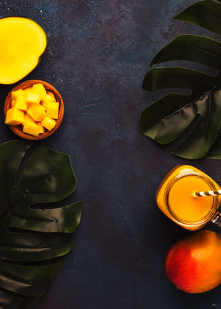 Mango smoothie in glass jar with fresh fruit on blue background, copy space, top view