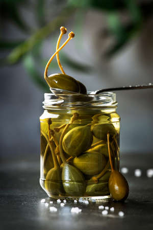 Capers. Marinated or pickled canned capers fruit close up in glass jar on gray kitchen table background. Copy spaceの写真素材
